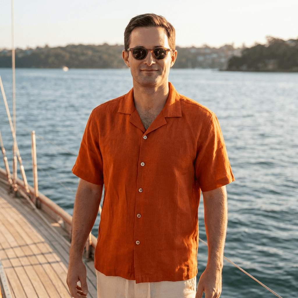 a photo of a man wearing a smart casual, camp collared hemp shirt made from terracotta coloured hemp fabric whilst standing on a yacht