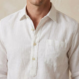 white button-up hemp shirt worn by a person on a beige background with focus on the chest pocket and quarter length placket