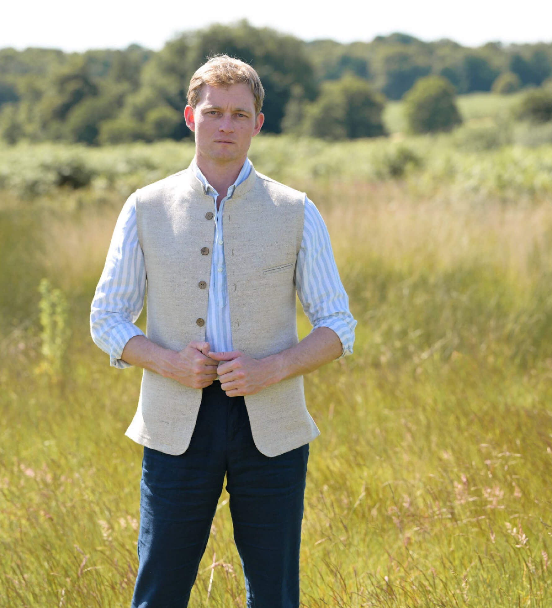 Man wearing a beige nehru gilet made from eco-friendly hemp fabric over a white shirt in a grassy field