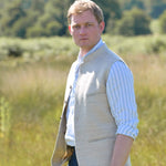 Man wearing a beige coloured sleeveless nehru jacket over a light blue shirt in a field with trees in the background