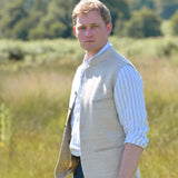 Man wearing a beige coloured sleeveless nehru jacket over a light blue shirt in a field with trees in the background