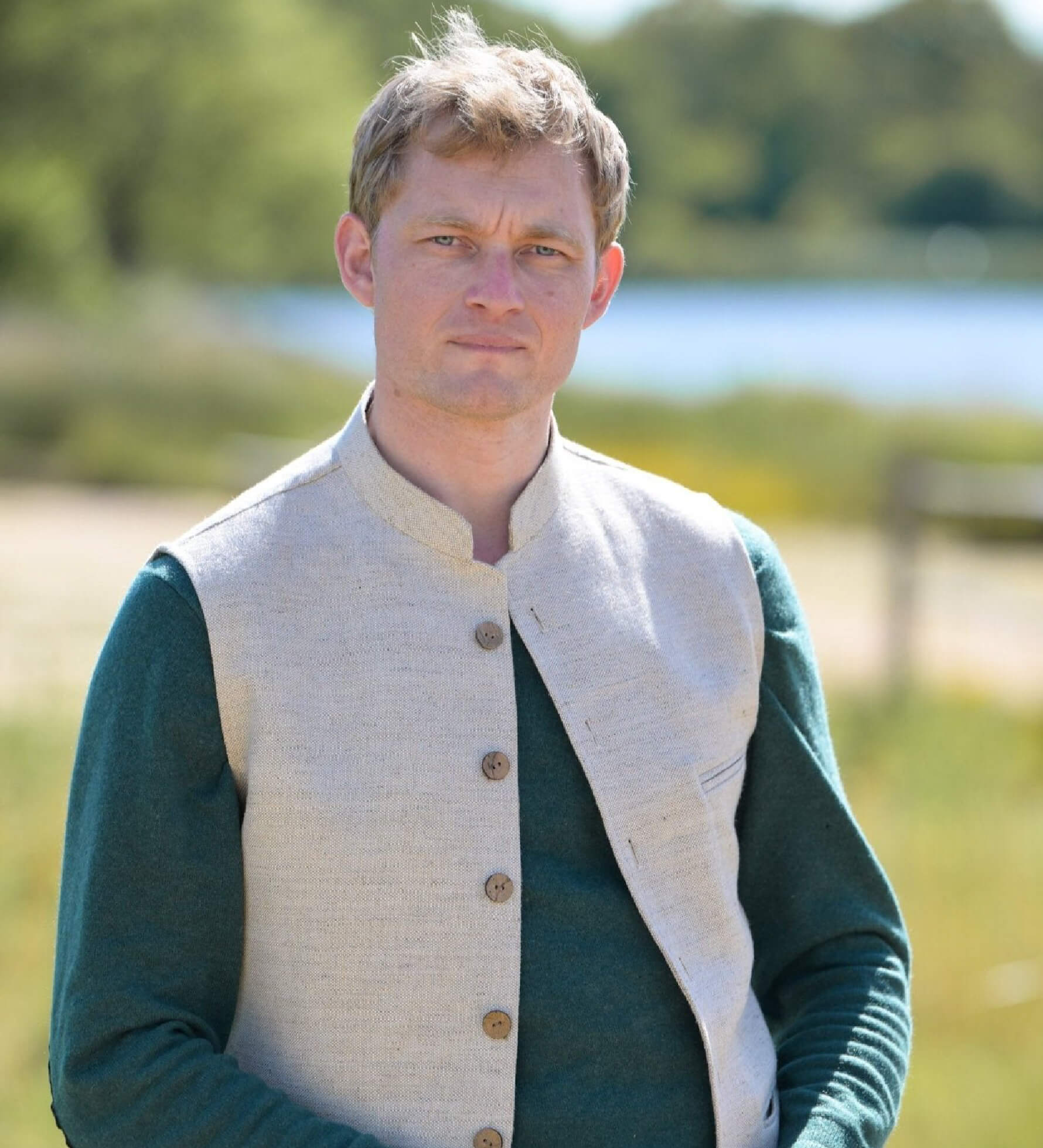 Man wearing a green jumper with cream nehru gilet outdoors with a blurred natural background