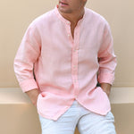 Man wearing a light pink button-up shirt  with mandarin collar and light blue jeans against a beige background