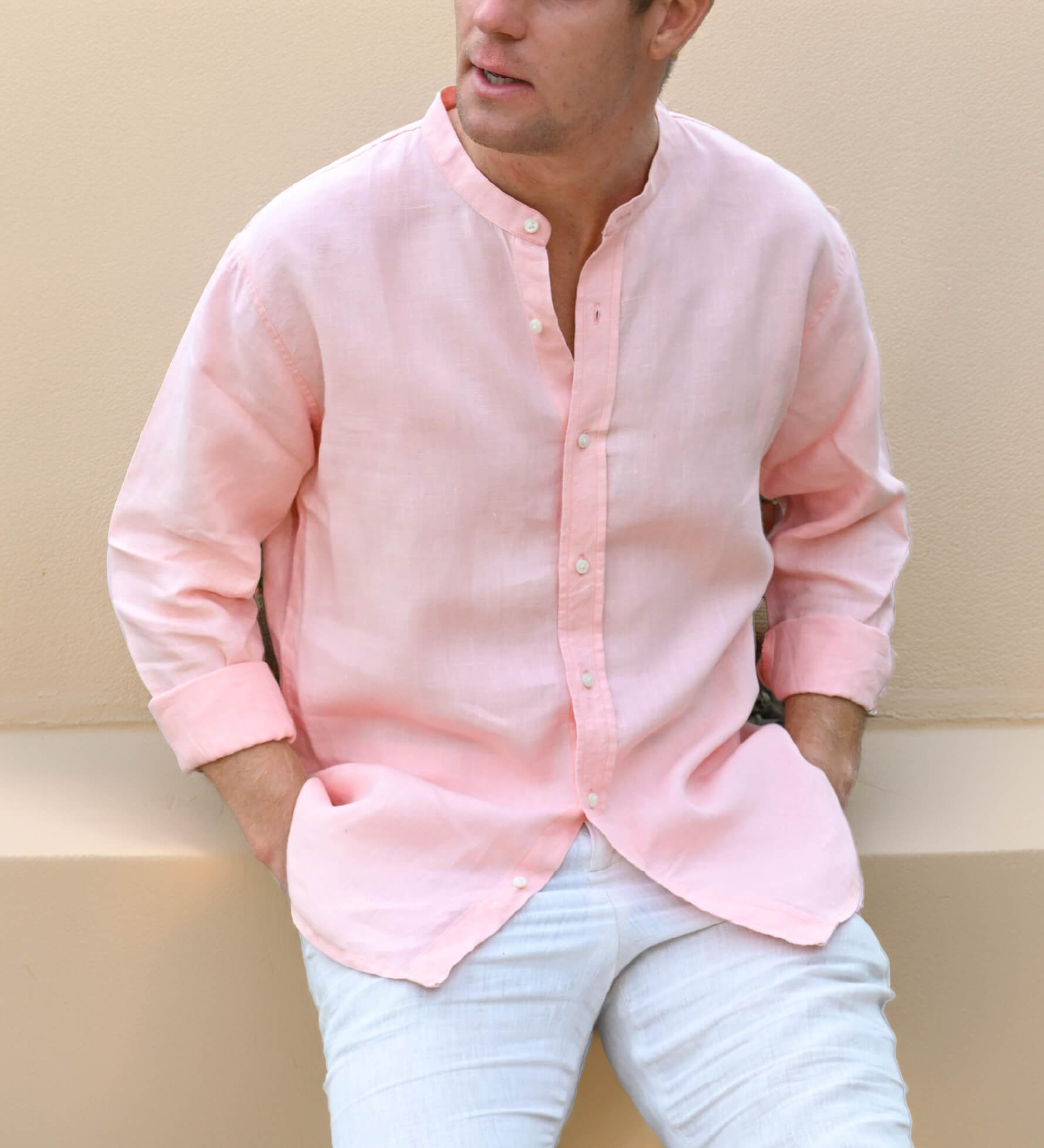 Man wearing a light pink button-up shirt  with mandarin collar and light blue jeans against a beige background