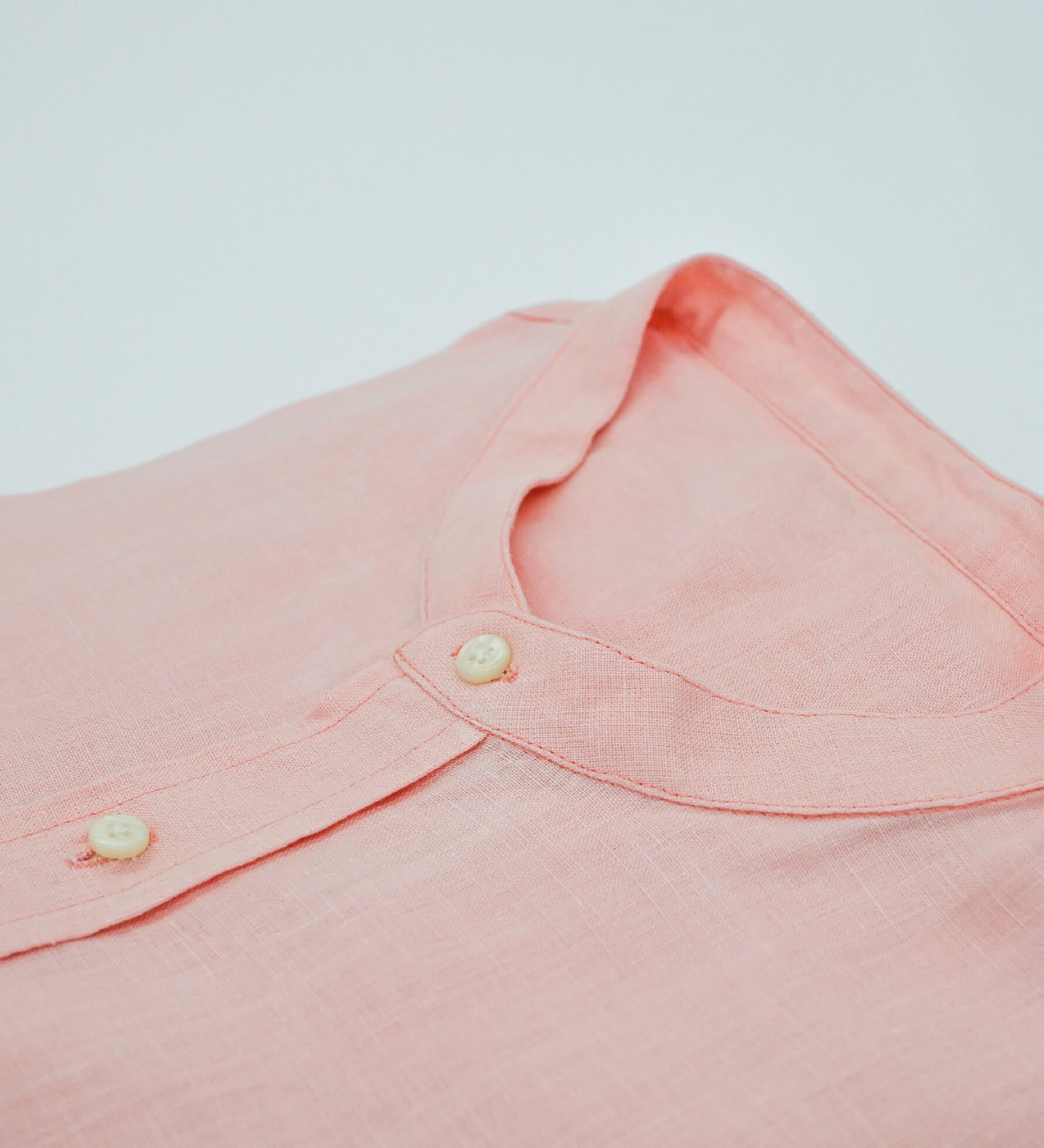 Close-up of a pinky peach hemp shirt collar with buttons on a light gray background