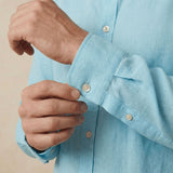 closeup shot of the cuff and button  being fastened on a hemp shirt colour light blue