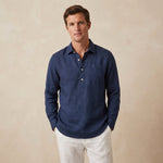 Man wearing a dark blue hemp fabric shirt and white trousers against a beige background