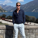 Man in sunglasses and a navy blue hemp shirt standing against a scenic backdrop of mountains and water.