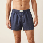 A man wearing dark blue hemp boxer briefs with an elastic waistband and a single button closure, shown from the chest down against a light beige background.