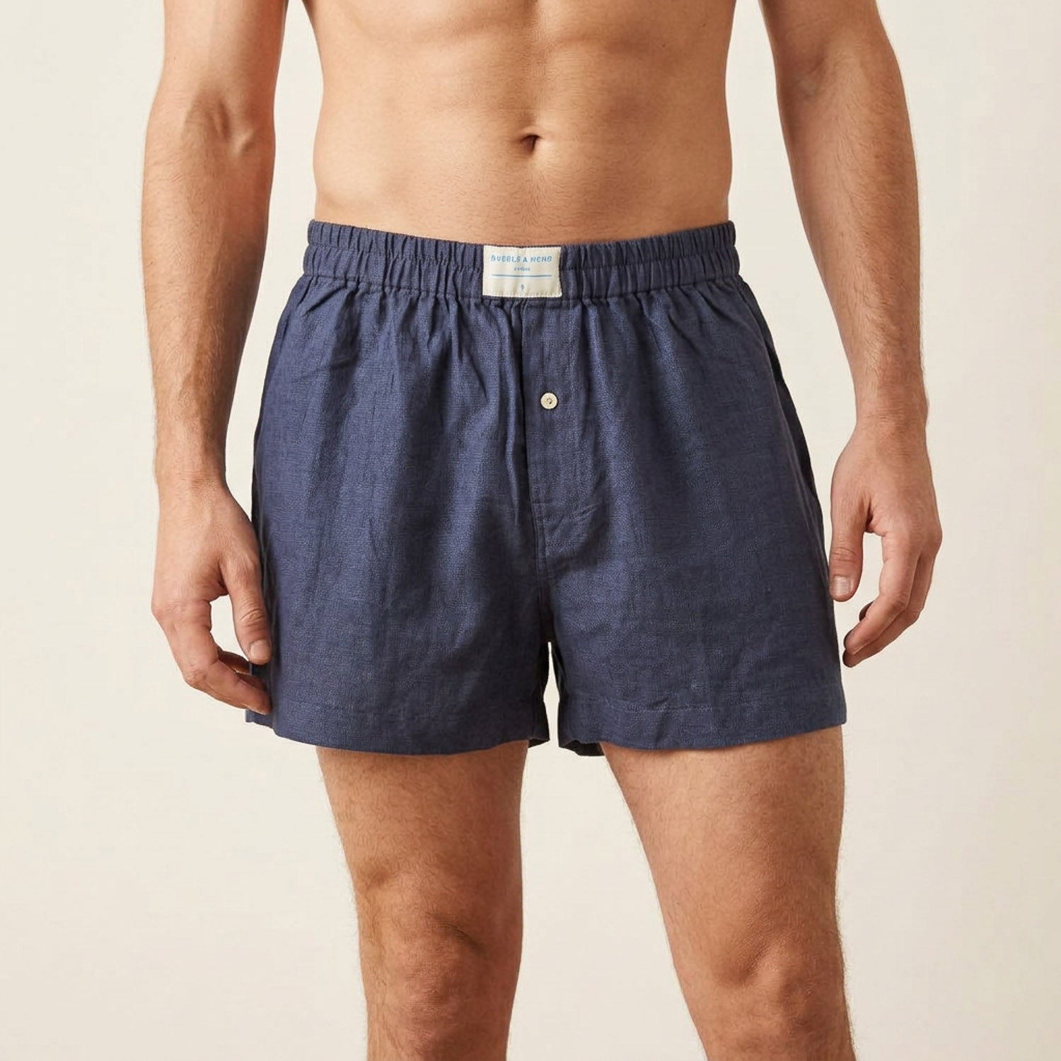 A man wearing dark blue hemp boxer briefs with an elastic waistband and a single button closure, shown from the chest down against a light beige background.