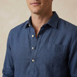 navy blue button-up hemp shirt worn by a person on a beige background with focus on the chest pocket and quarter length placket