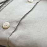 Close-up of a light gray shirt with buttons on a blurred background. The closeup shows the softness and texture of the fine hemp fabric.