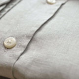 Close-up of a light gray shirt with buttons on a blurred background. The closeup shows the softness and texture of the fine hemp fabric.