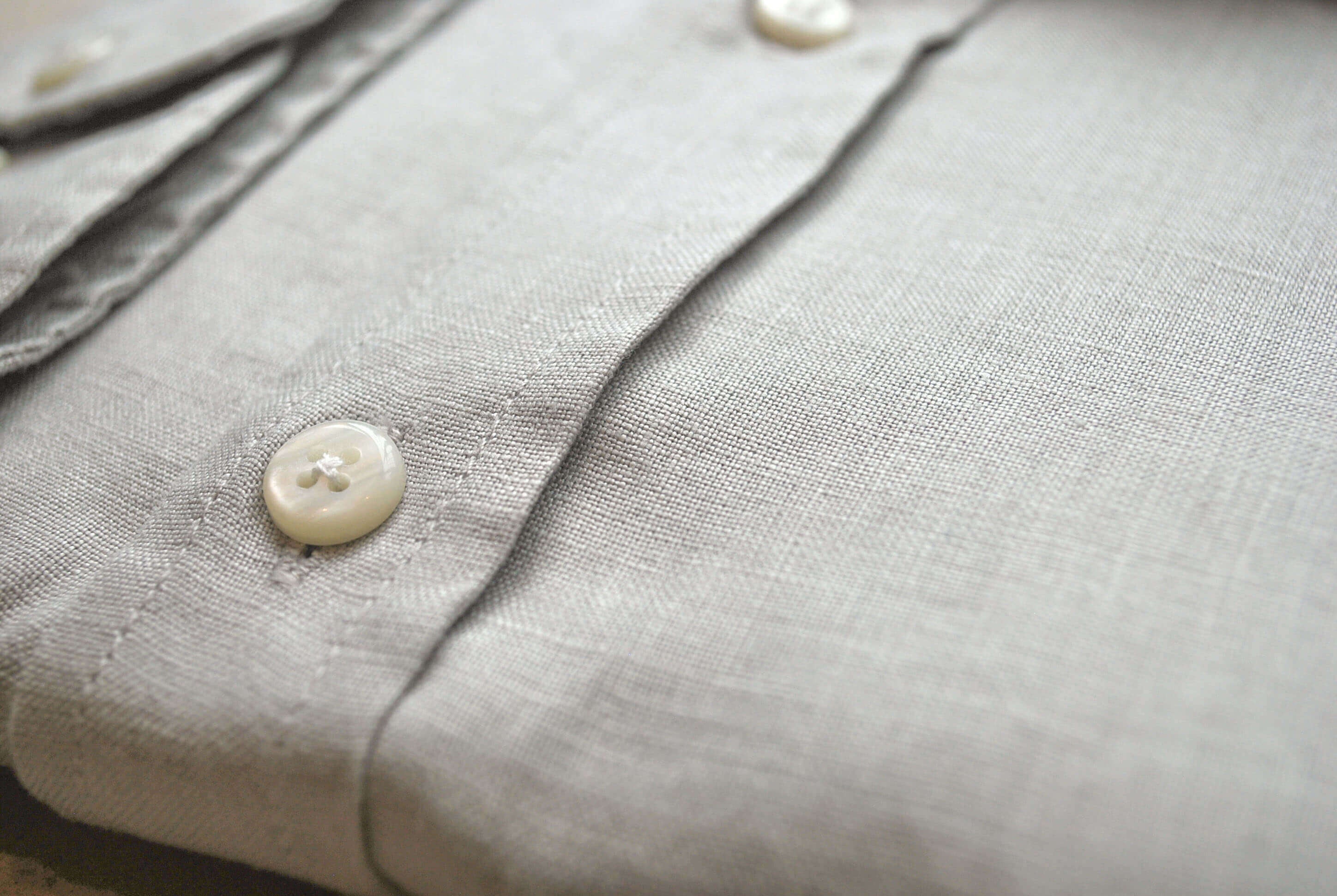 Close-up of a light gray shirt with buttons on a blurred background. The closeup shows the softness and texture of the fine hemp fabric.