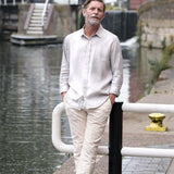 Man in light-colored shirt and pants standing by a canal with buildings in the background
