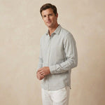 a man wears a light grey shirt made from hemp fabric whilst standing in front of a beige backdrop