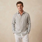 a man wears a light grey shirt made from hemp fabric whilst standing in front of a beige backdrop