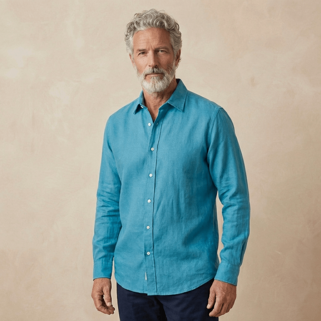 a man models a petrol blue shirt made from hemp fabric set against a beige wall behind