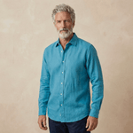 a man models a petrol blue shirt made from hemp fabric set against a beige wall behind