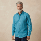 a man models a petrol blue shirt made from hemp fabric set against a beige wall behind