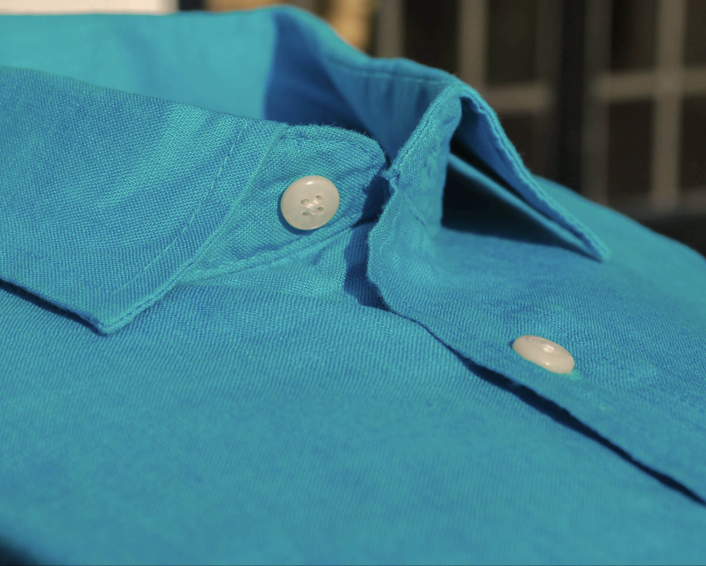 Close-up of a blue shirt collar with buttons against a blurred background