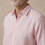 A close-up of a man wearing a light pink and white gingham check  shirt, showing the collar, front buttons, and textured fabric.
