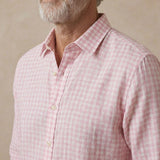 A close-up of a man wearing a light pink and white gingham check  shirt, showing the collar, front buttons, and textured fabric.