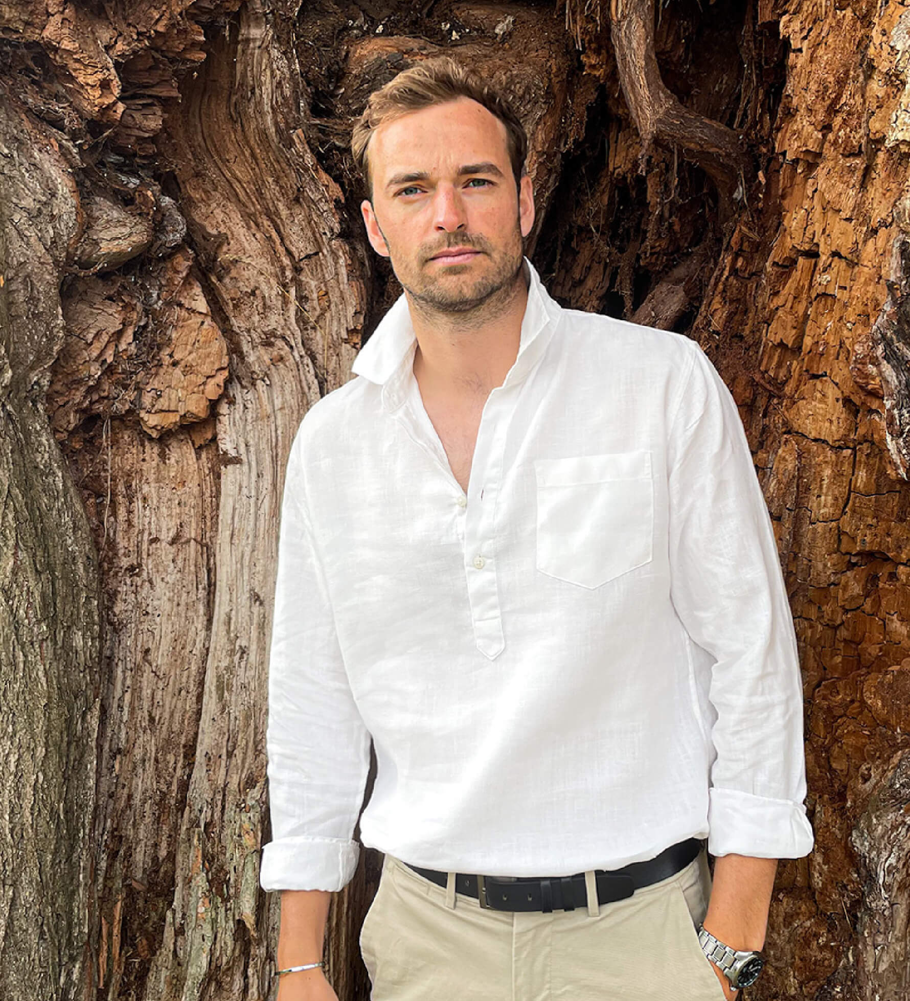 Man wearing a white hemp shirt in a popover style and chest pocket standing against a textured wooden background