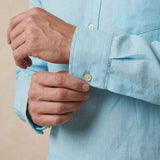 closeup shot of the cuff and button being fastened on a hemp shirt with pocket light blue