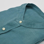 Close-up of a teal hemp shirt with button details on a light gray background
