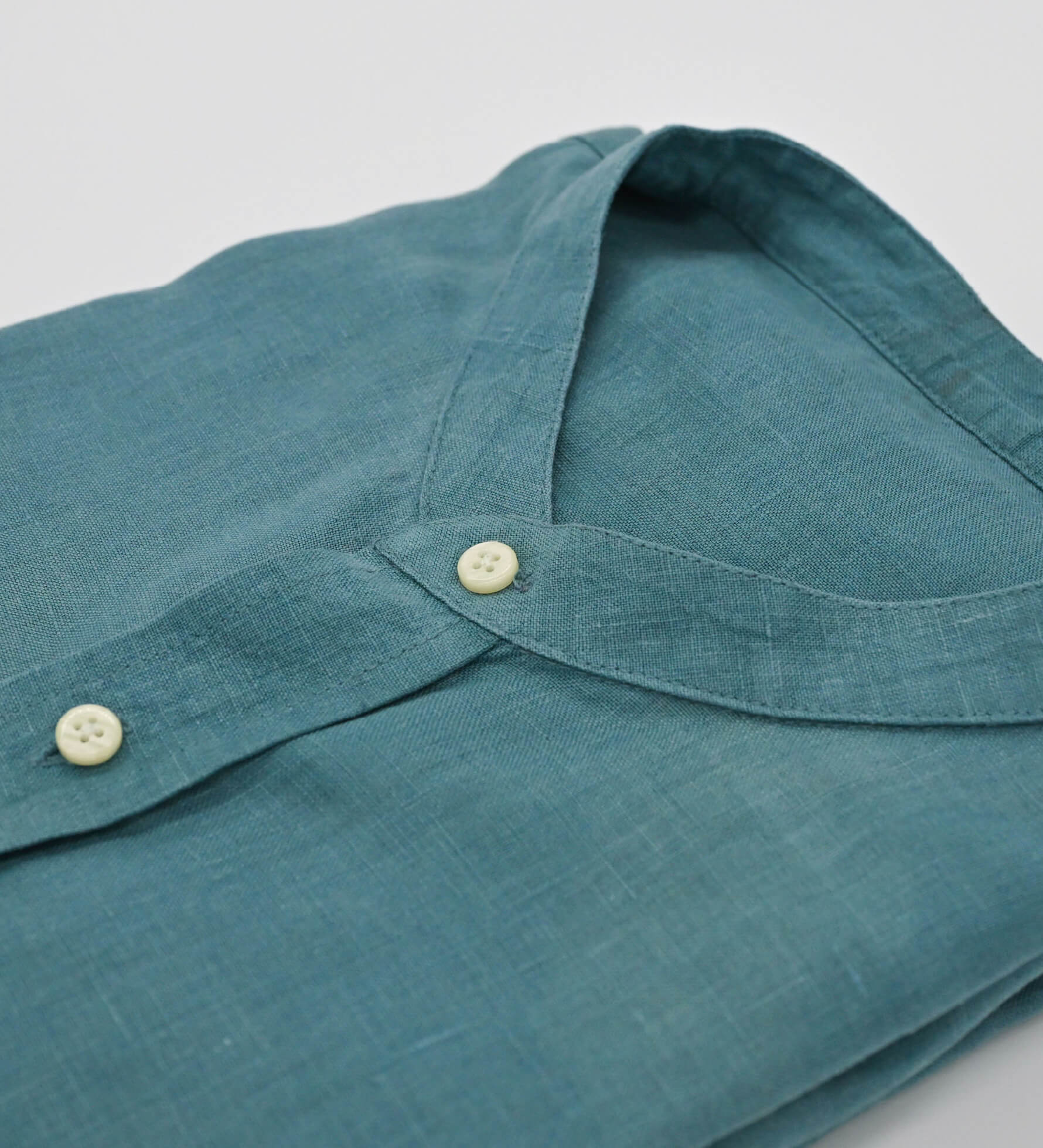 Close-up of a teal hemp shirt with button details on a light gray background