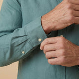 closeup shot of the cuff and button being fastened on a hemp shirt with grandad collar colour blue