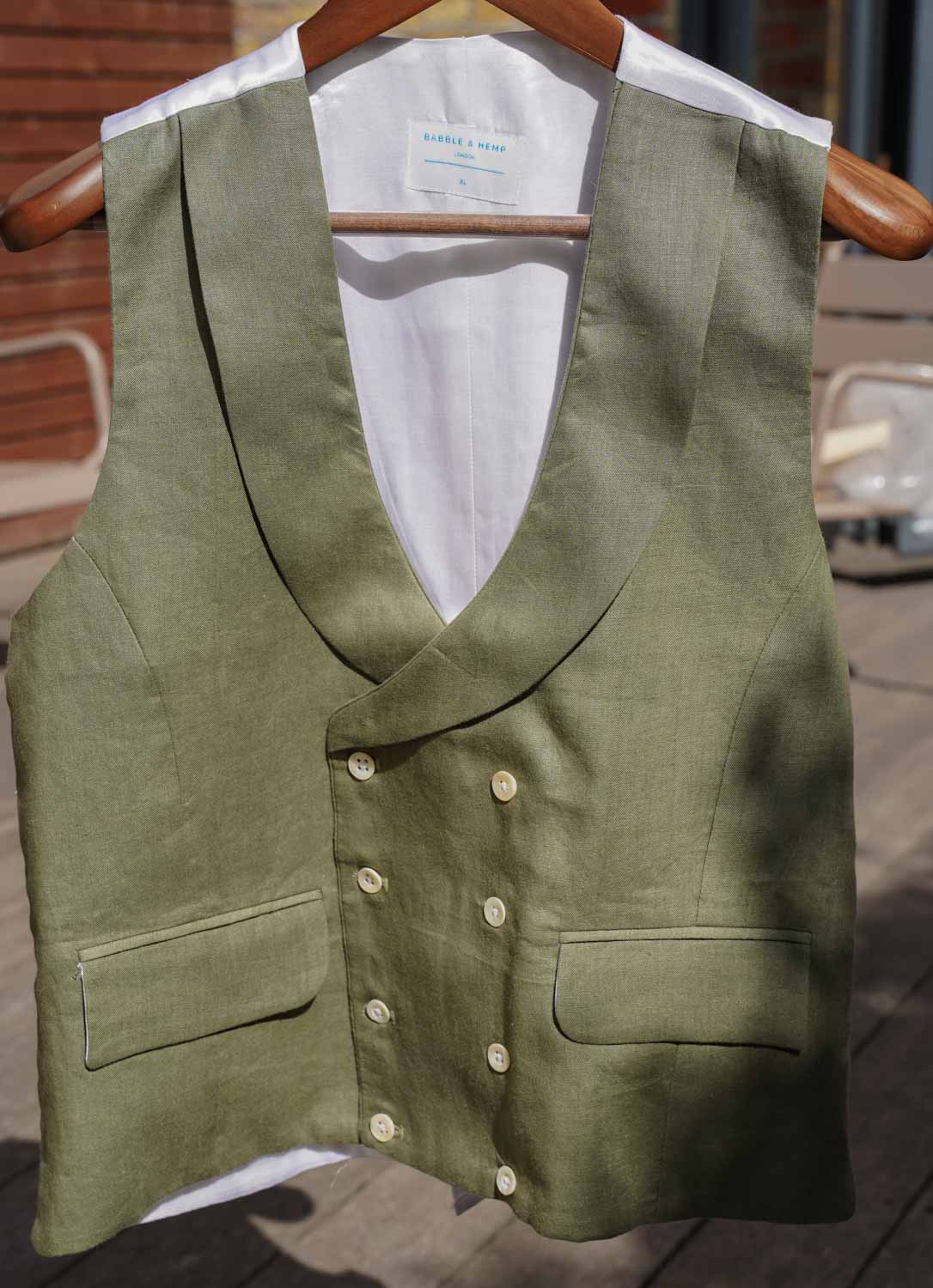 a formal green hemp waistcoat worn for weddings or royal ascot hangs from a wooden hanger