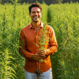 Man holding a plant in a field of greenery wearing a terracotta coloured hemp shirt