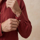 Close-up of a person wearing a textured burgundy long-sleeve soft hemp shirt and adjusting the button on the cuff with both hands.
