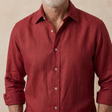 A close-up of a man wearing a textured red hemp button-down shirt with rolled-up sleeves, set against a neutral beige background.