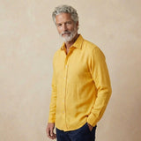 man wears yellow hemp shirt in heavy weight of fabric in front of beige backdrop 