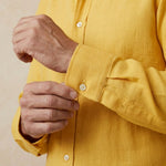 closeup shot of the cuff and button  being fastened on a hemp shirt colour yellow