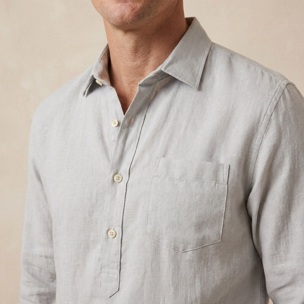 Light gray button-up hemp shirt worn by a person on a beige background with focus on the chest pocket and quarter length placket