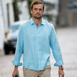 Man wearing a light blue shirt and beige pants walking outdoors.