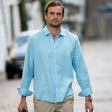 Man wearing a light blue shirt and beige pants walking outdoors.