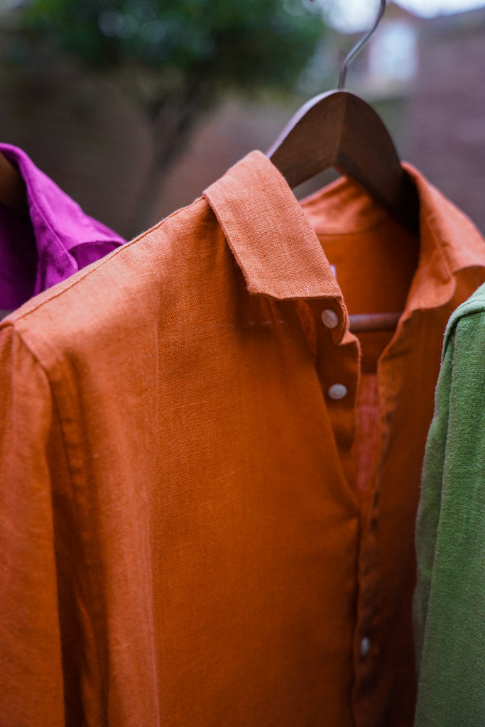 a closeup shot showing the detail and soft texture of a terracotta coloured hemp shirt hanging from a shirt hanger
