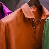 a closeup shot showing the detail and soft texture of a terracotta coloured hemp shirt hanging from a shirt hanger