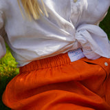 Person wearing a white shirt and orange hemp boxer shorts with a visible brand Babble & Hemp label, sitting on grass.